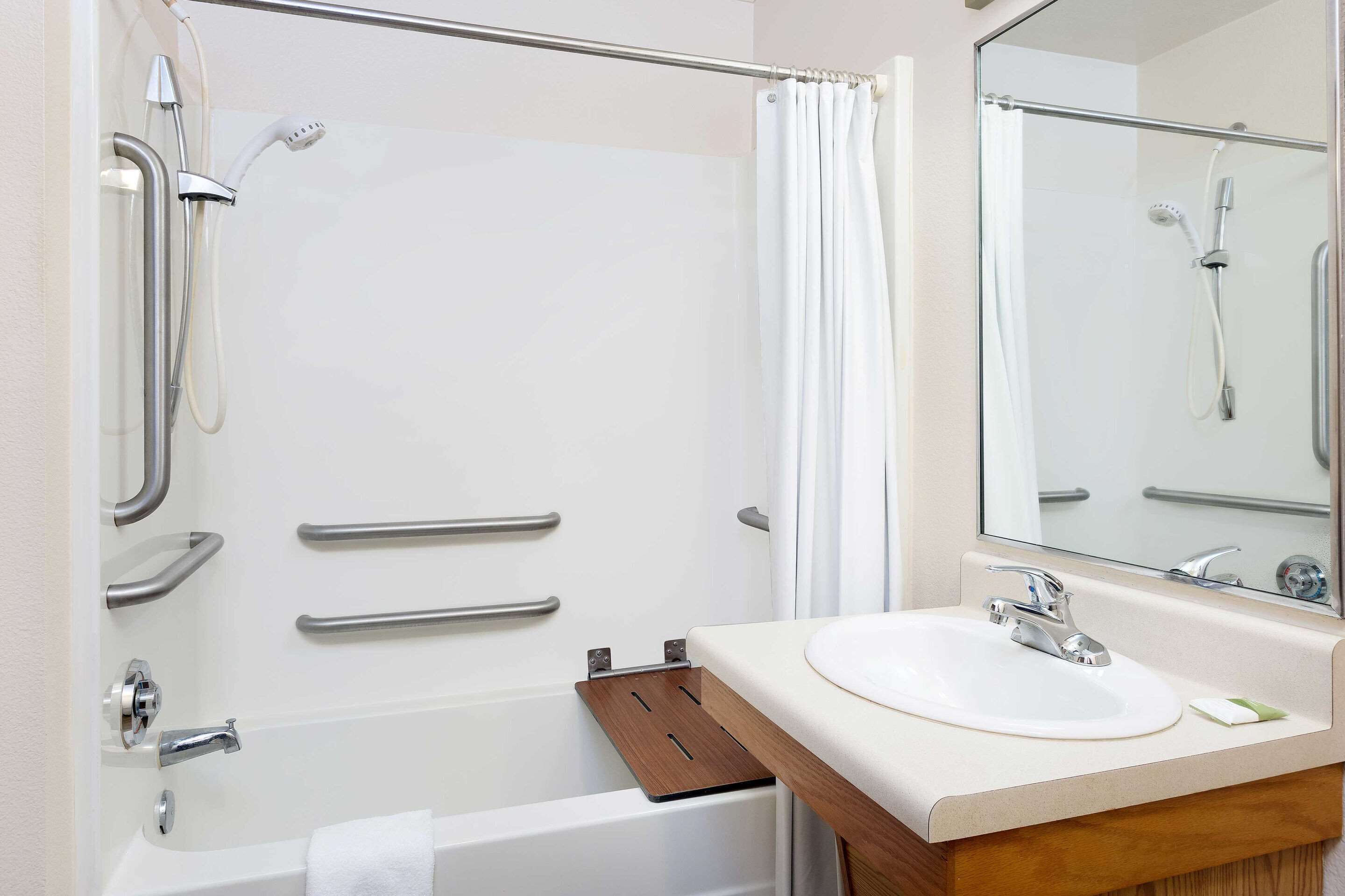 Un bagno moderno con doccia, maniglie di sostegno, vasca da bagno e lavandino con specchio.
