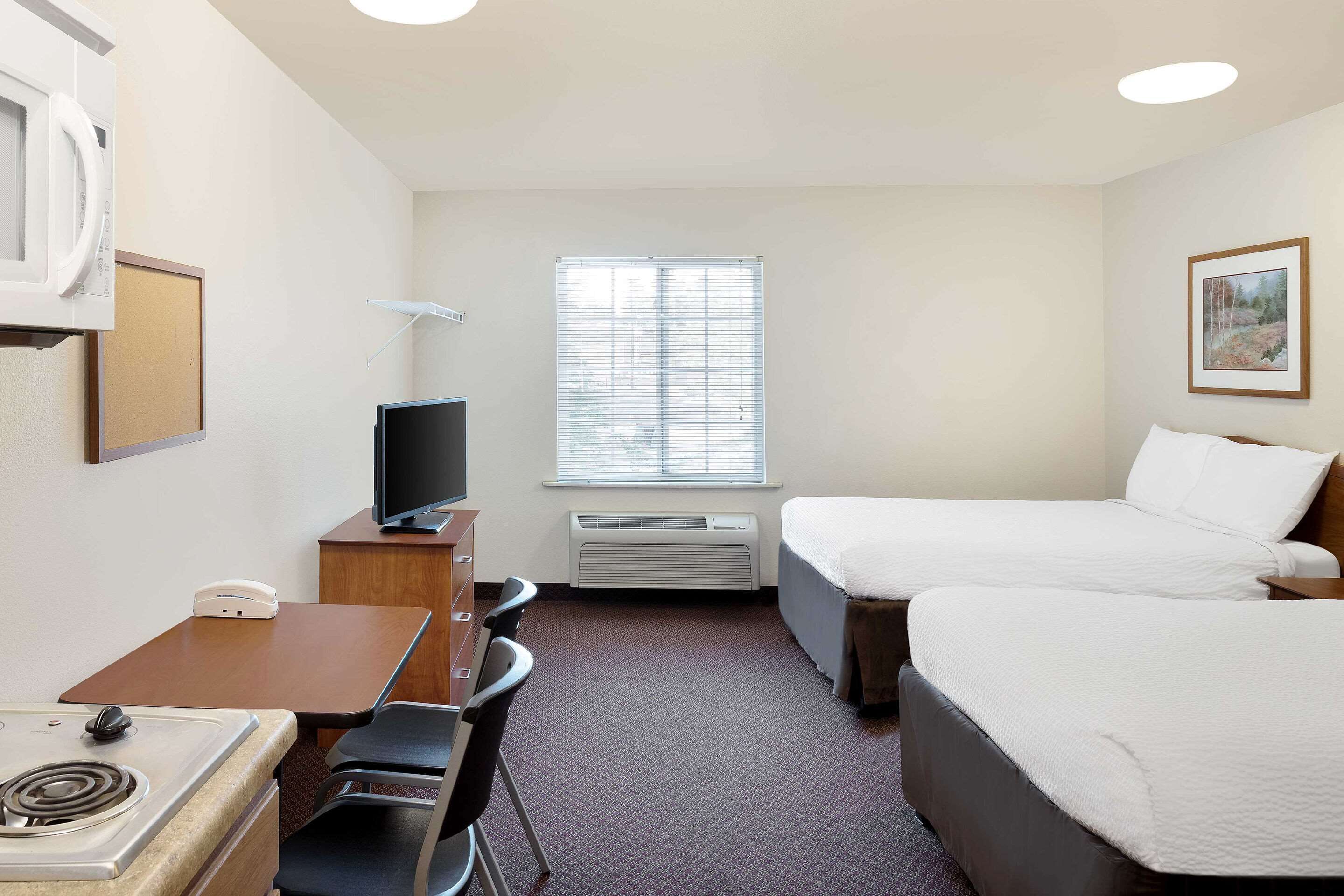 A hotel room with two beds, a desk with a computer, a microwave, and a TV.