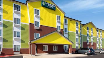 A multi-story hotel with a yellow and green facade, a covered entrance, and a parking lot with cars.