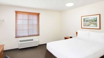 A hotel room with a bed, a window with blinds, a picture on the wall, and a heater on the floor.