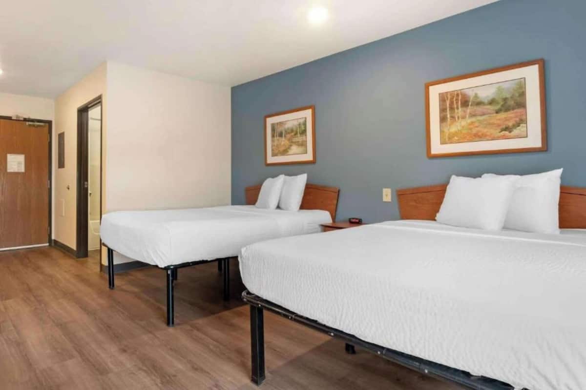 A hotel room with two single beds, wooden headboards, a door, and two framed pictures on the wall.