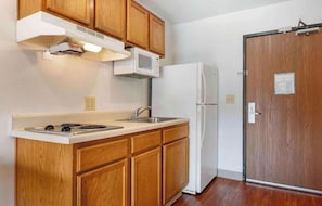 A compact kitchen with wooden cabinets, a white stove, a microwave, and a refrigerator. - Studio 6 Extended Stay Cincinnati Sharonville OH (Sharonville)