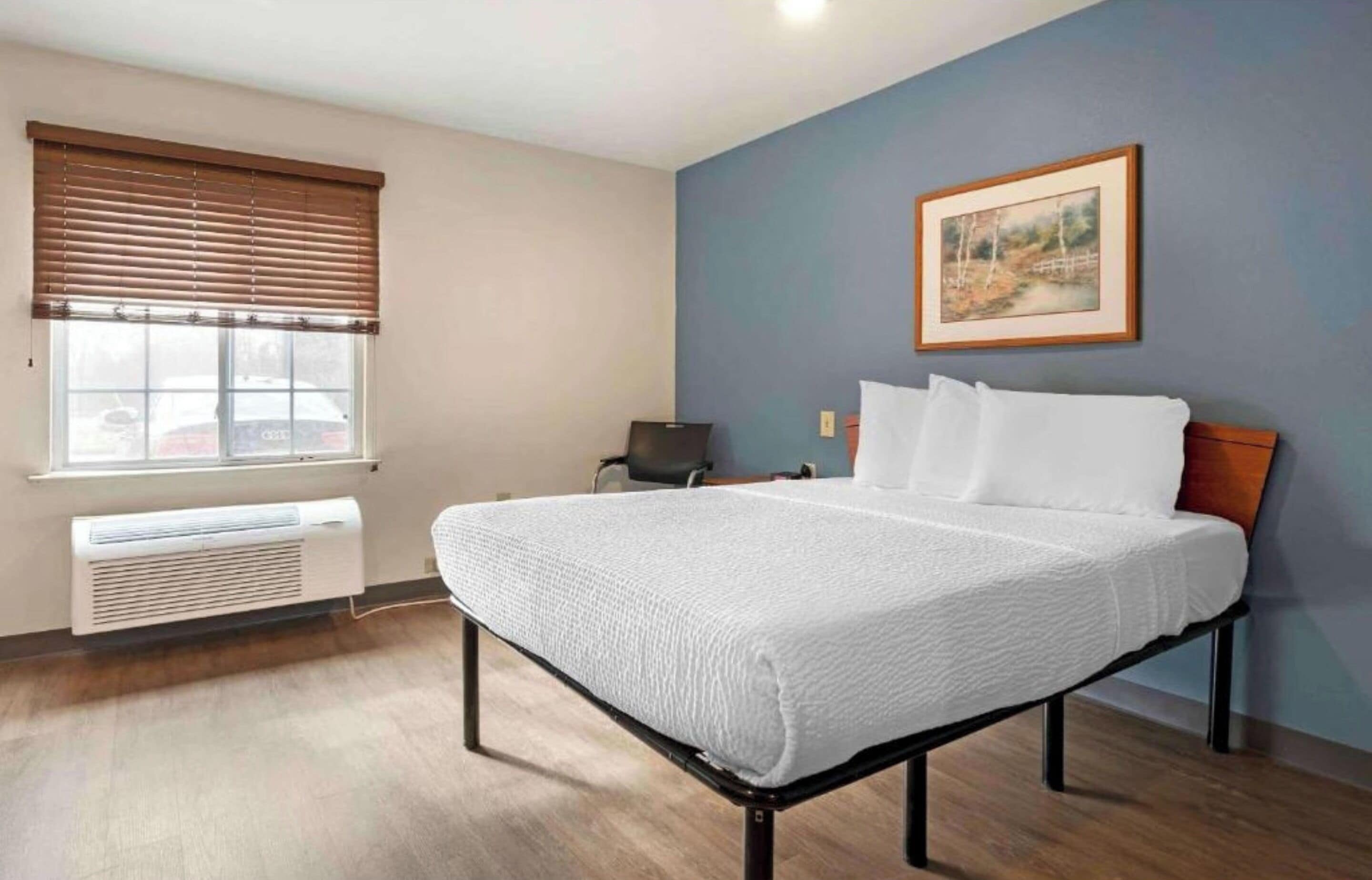A bedroom with a bed, a window with blinds, a radiator, and a painting on the wall.