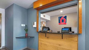 Una recepción con un cartel que indica la disponibilidad de habitaciones, una planta y un estante pequeño.