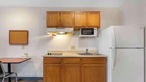 Une cuisine compacte avec des meubles en bois, un four à micro-ondes, un réfrigérateur, une petite table et une chaise.