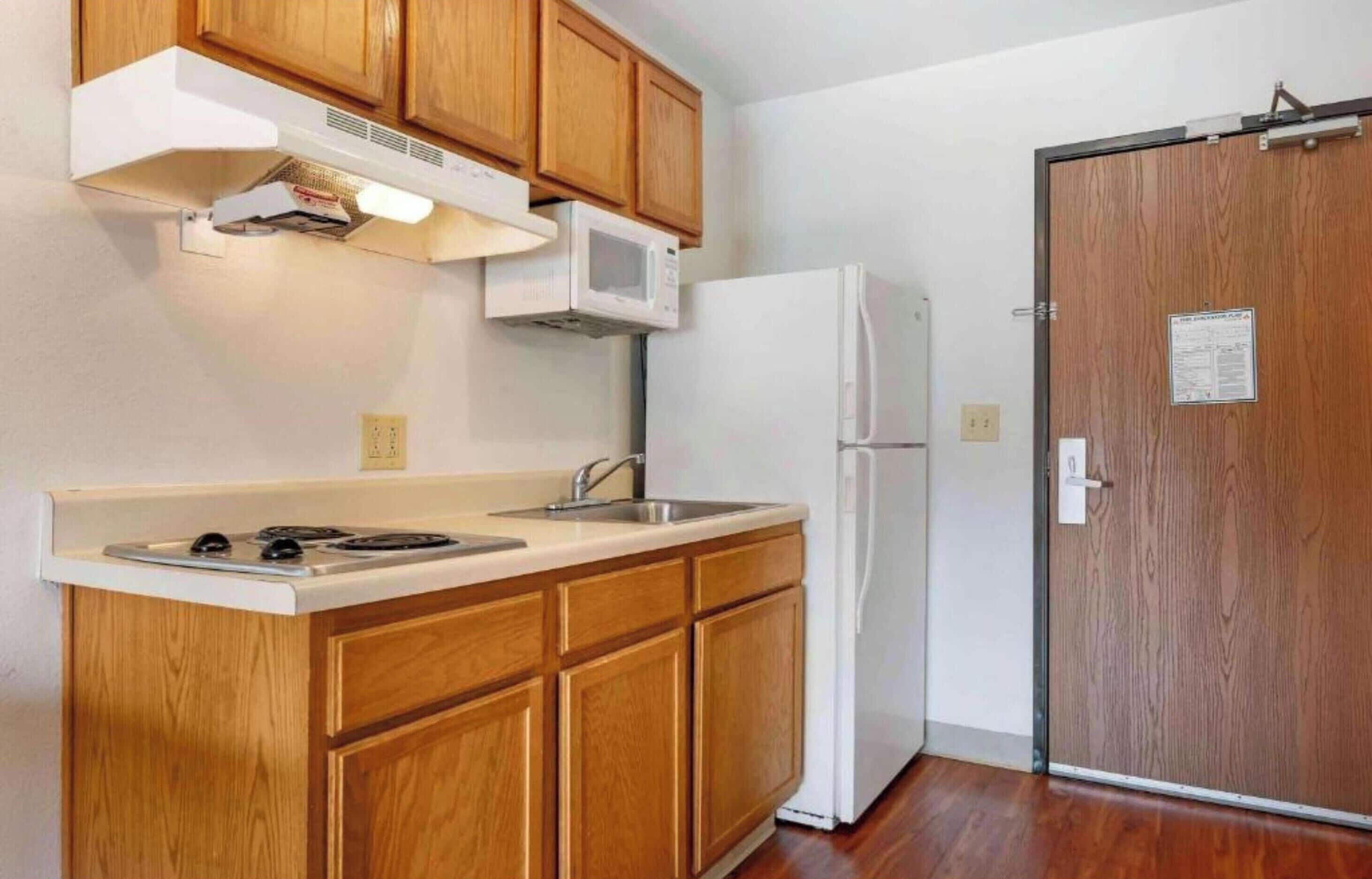 A compact kitchen with wooden cabinets, a microwave, a refrigerator, and a sink.