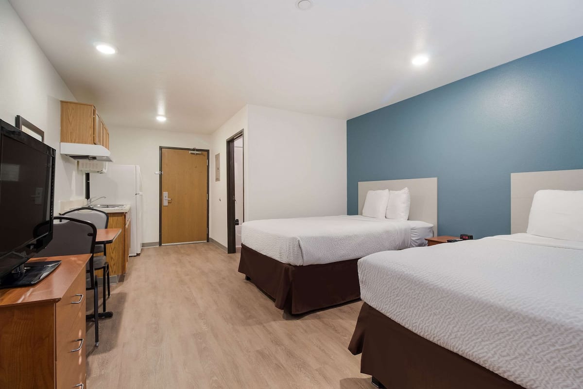 A hotel room with two beds, a desk with a computer, a television, and a kitchenette.