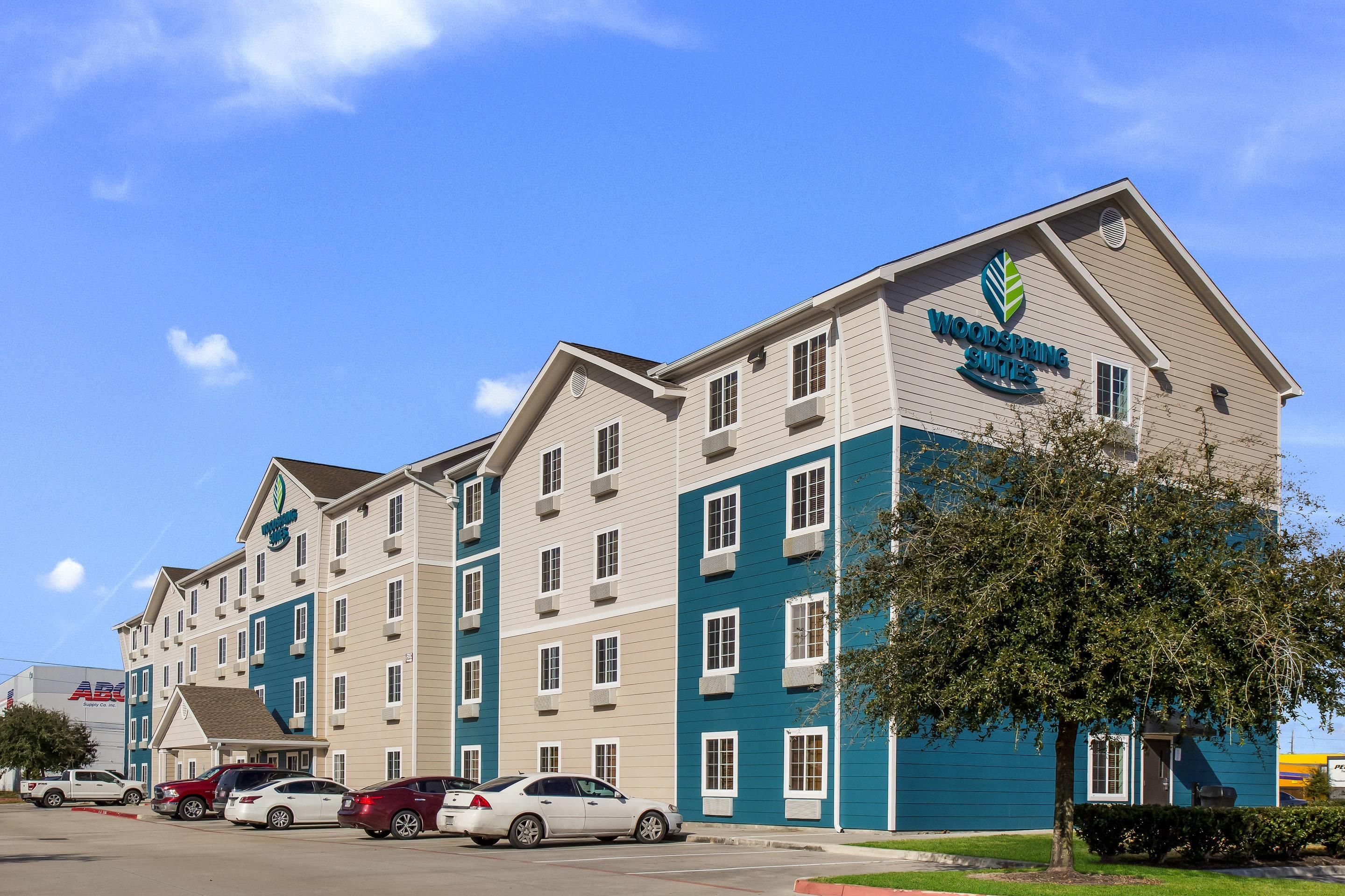A multi-story hotel with a sign for 'Woodspring Suites' and a parking lot with several cars.