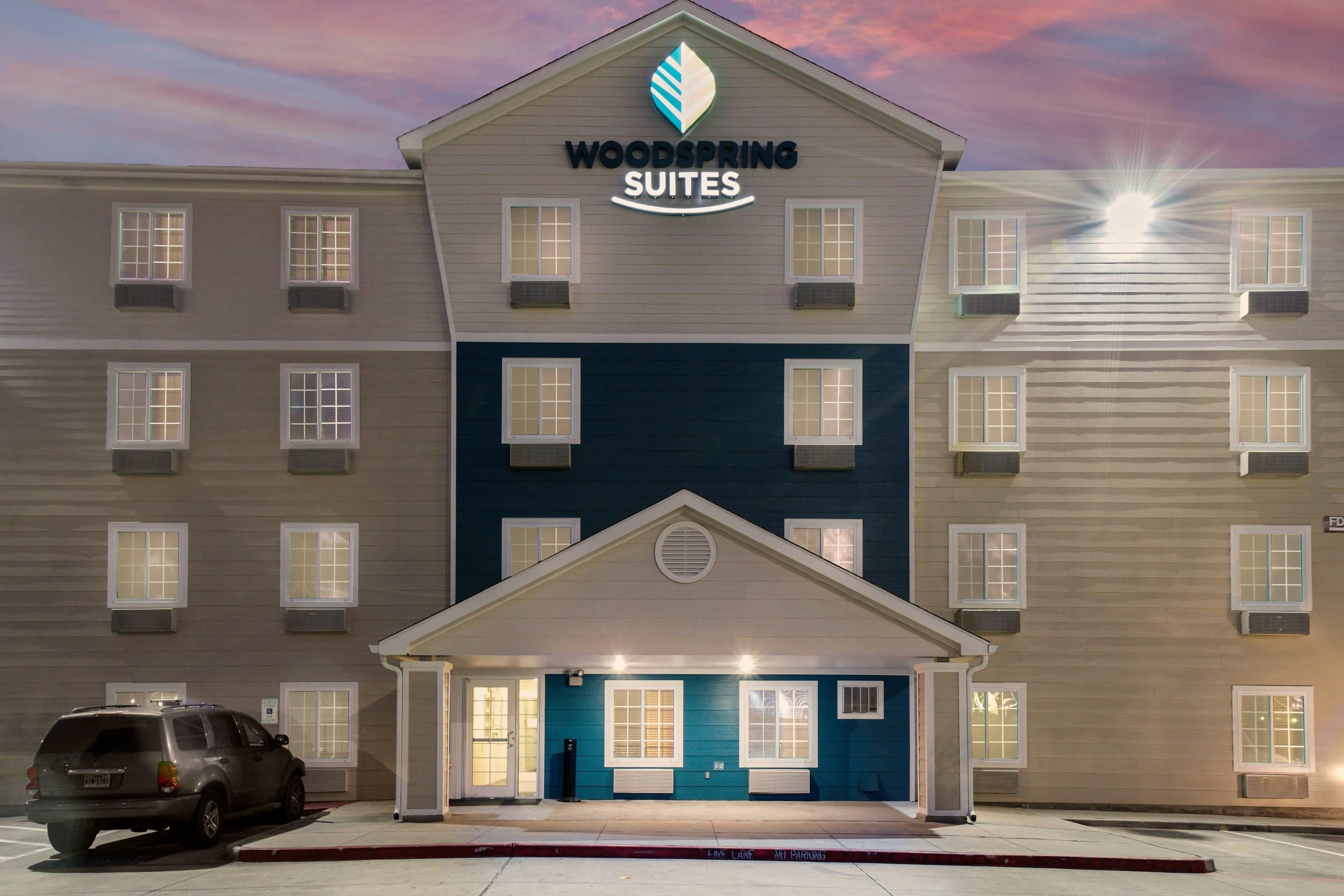 A multi-story hotel with a sign reading 'Woodspring Suites' and a covered entrance.