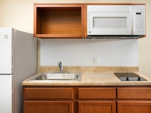 A kitchen with a built-in microwave, a stainless steel sink, and wooden cabinets. - WoodSpring Suites Houston I-45 Airtex (Houston)