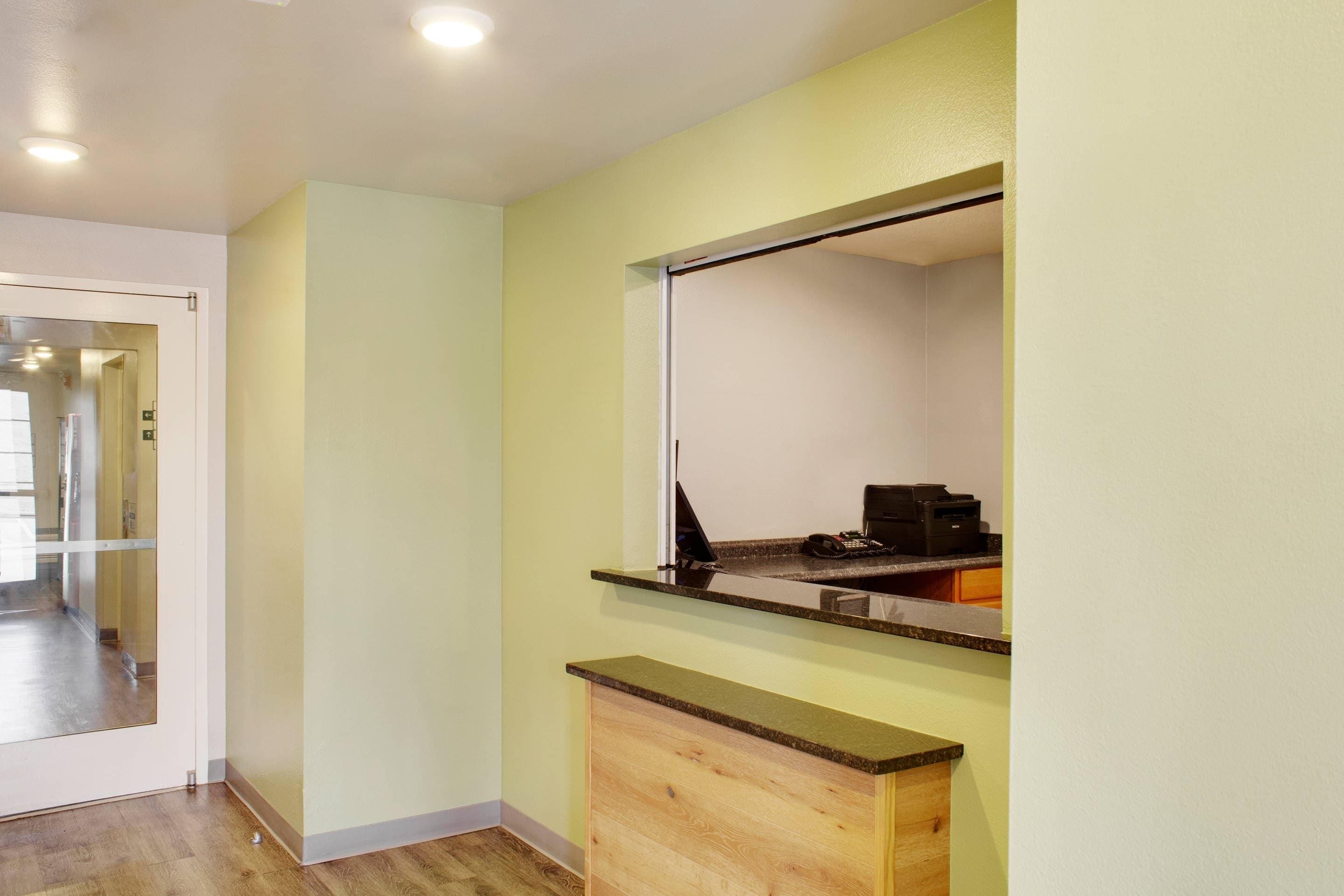 Una habitación con un escritorio de madera, un espejo y una puerta que da a otra zona.