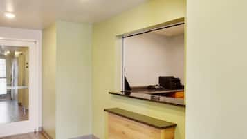 Una habitación con un escritorio de madera, un espejo y una puerta que da a otra zona.