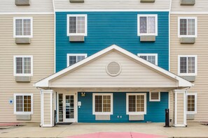 A multi-story building with a central entrance featuring a blue facade and white trim. - WoodSpring Suites Conroe (Conroe)