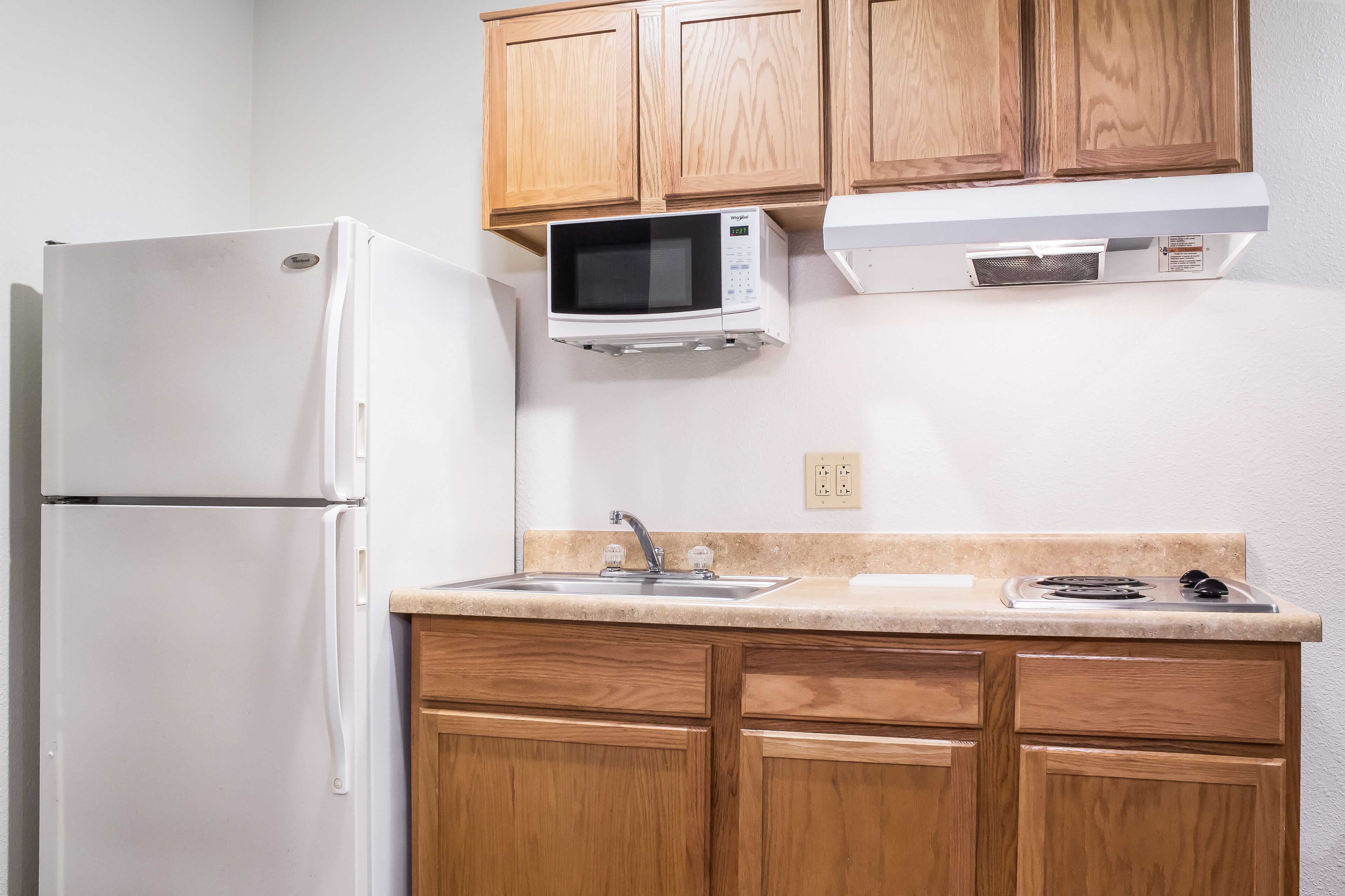 Una cocina con armarios de madera, un refrigerador blanco, un microondas, un lavamanos y una estufa.