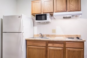 A kitchen with wooden cabinets, a white refrigerator, a microwave, a sink, and a stove. - WoodSpring Suites Conroe (Conroe)