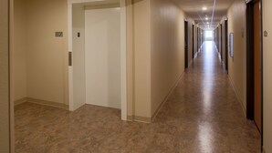 A long, narrow hallway with beige walls and a brown floor, leading to multiple doors.