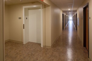 Un pasillo largo y estrecho con paredes color beige y piso marrón, que conduce a varias puertas.