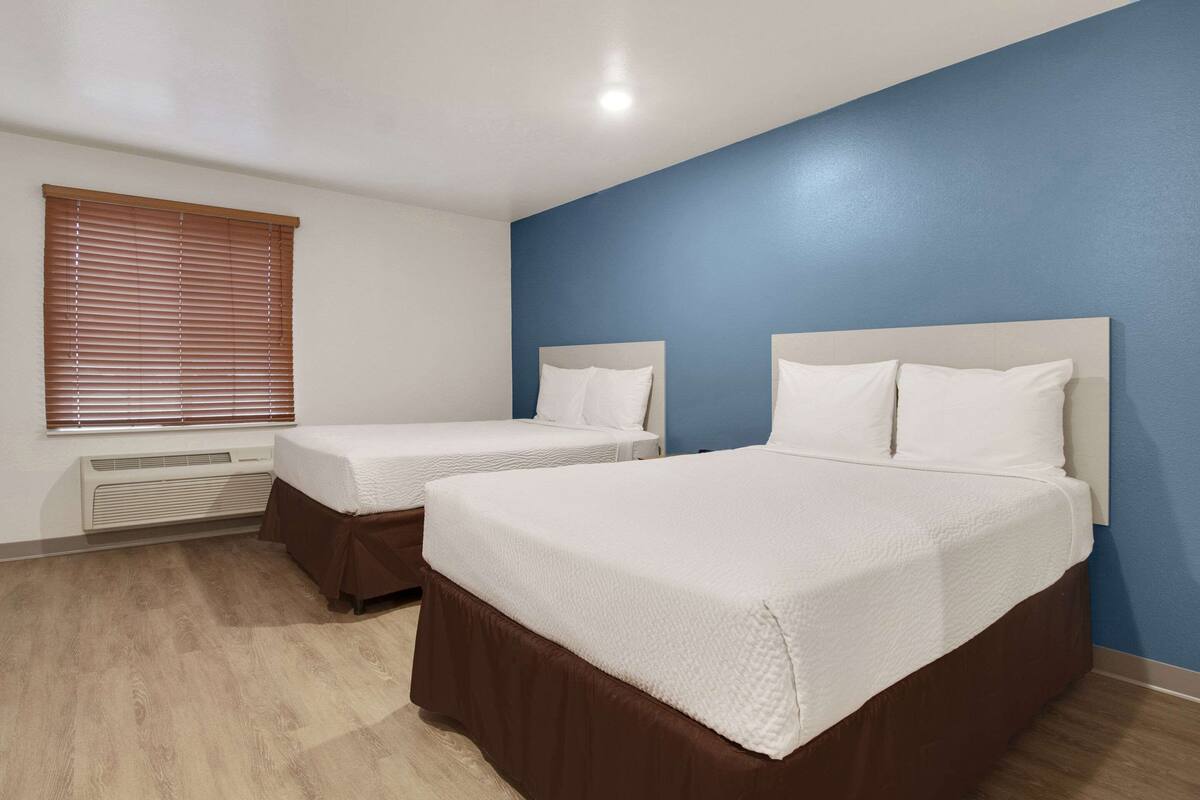 Ett hotellrum med två sängar, ett fönster med persienner, en värmare och en blå accentvägg.
