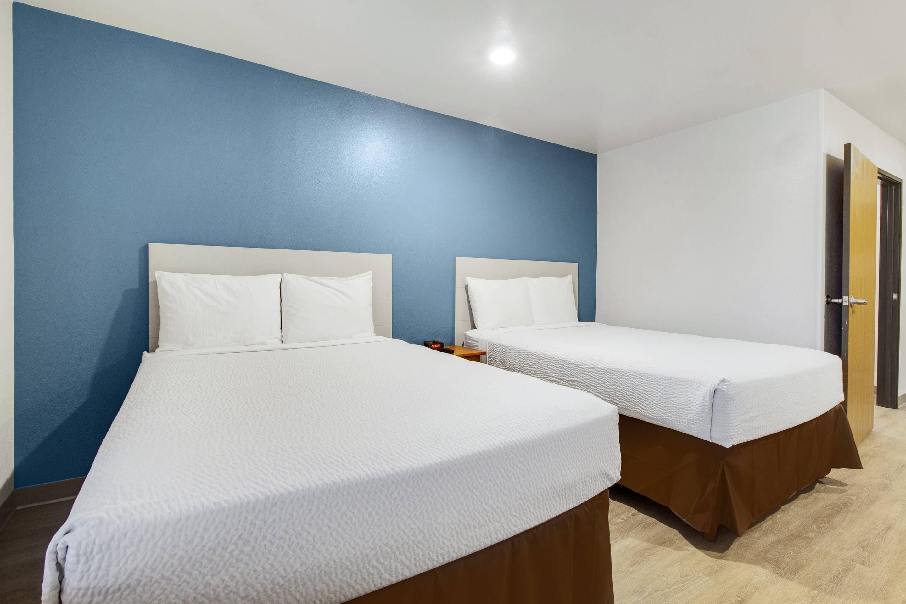 Habitación de hotel con dos camas, suelo de madera y pared azul.