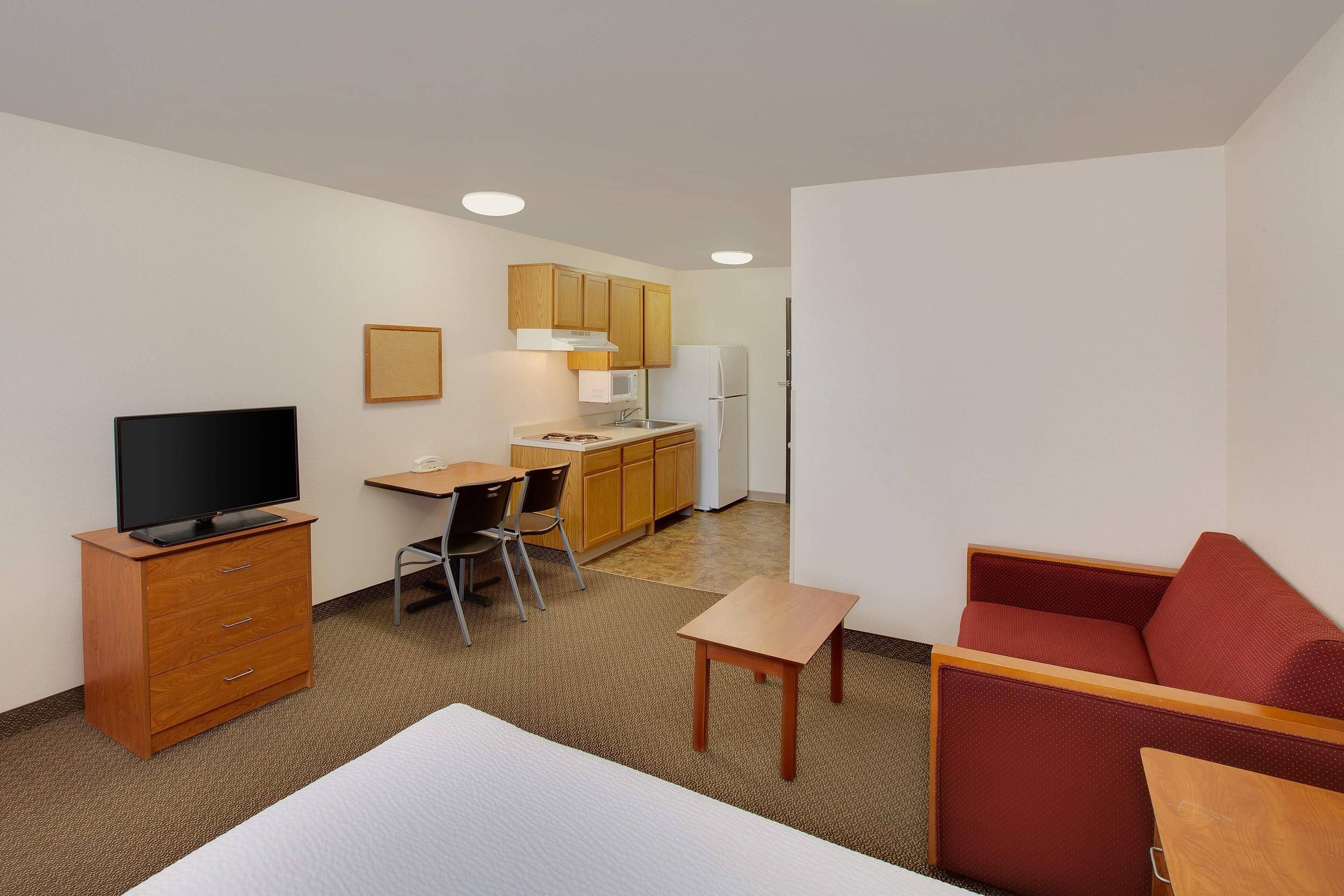 Habitación de hotel compacta con cama, escritorio con silla, kitchenette y televisión.