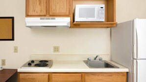 A compact kitchen with wooden cabinets, a built-in microwave, a stove, and a refrigerator. - WoodSpring Suites Houston I-10 West (Houston)
