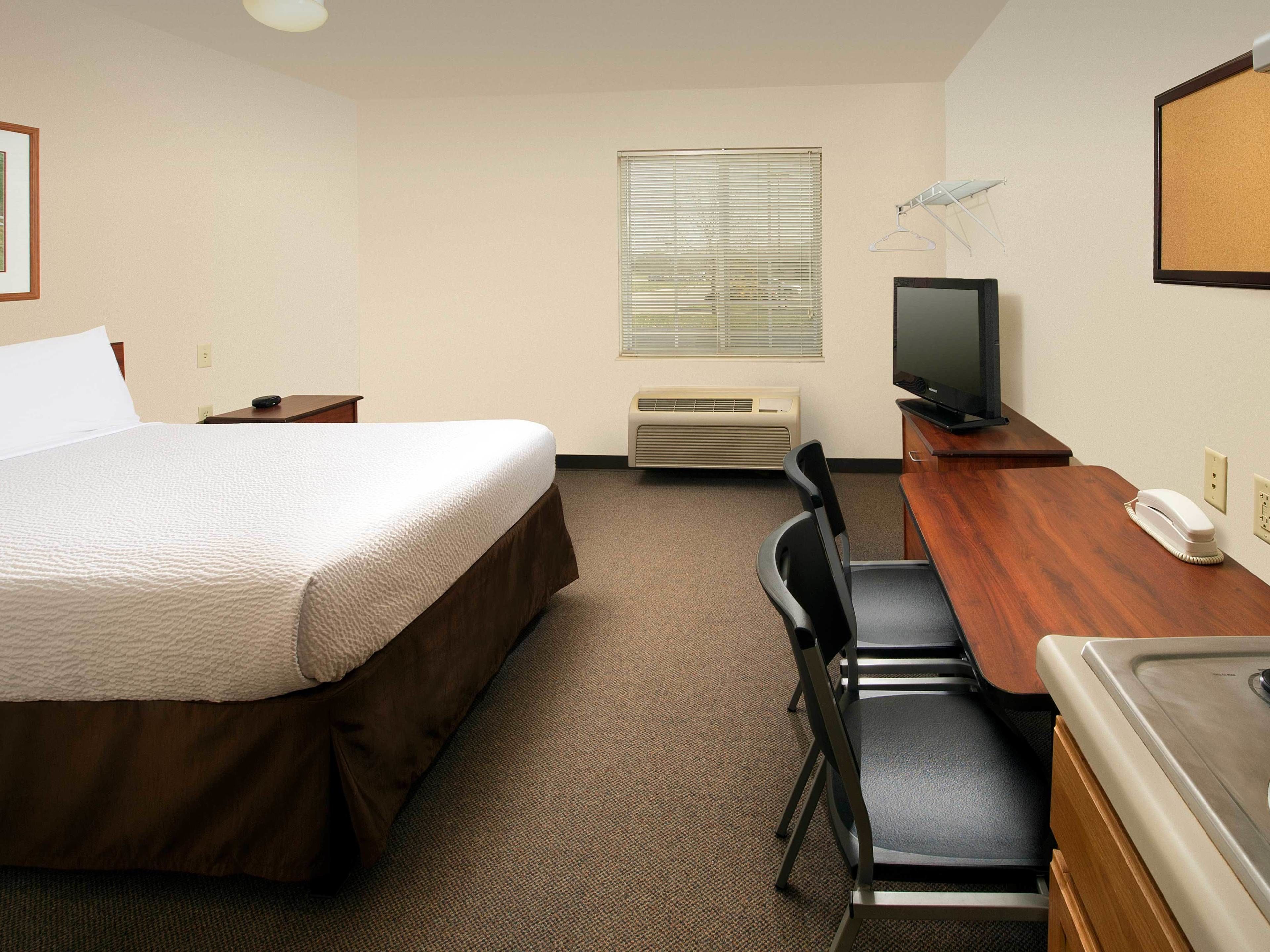 A hotel room with a bed, a desk with a chair, a television, and an air conditioning unit.