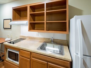 A compact kitchen with wooden cabinets, a built-in microwave, a sink, and a white refrigerator. - WoodSpring Suites Houston Willowbrook (Houston)