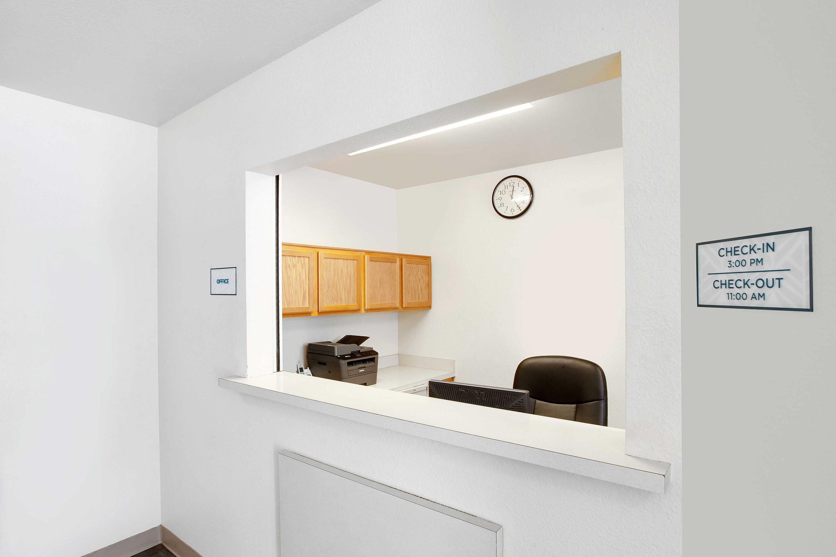 A reception desk with a clock, a sign indicating check-in and check-out times, and wooden cabinets in the background.