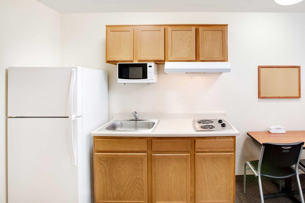 A compact kitchenette with a refrigerator, microwave, sink, stove, and wooden cabinets.
