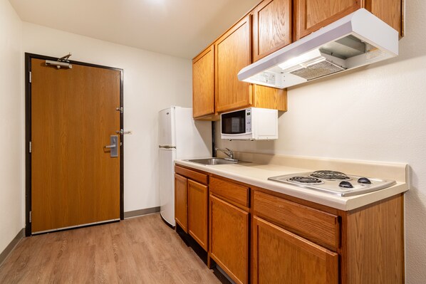 Una cocina compacta con armarios de madera, un microondas, un refrigerador y una estufa.