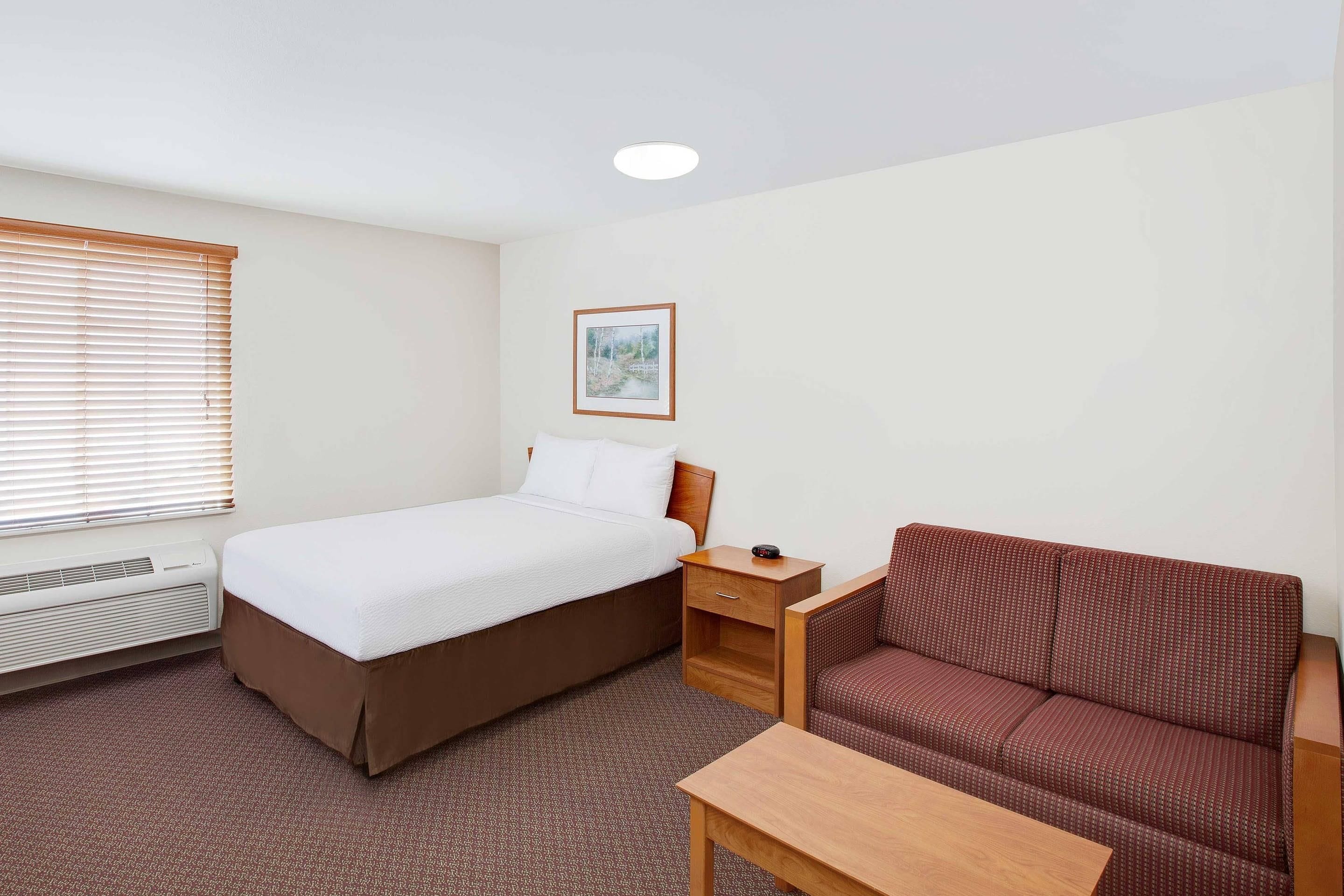 A hotel room with a bed, a bedside table with a radio, a sofa, and a small table.