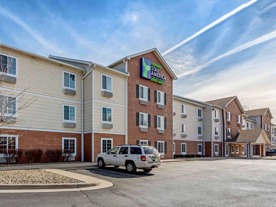 Ein mehrstöckiges Hotel mit einem gut sichtbaren Schild 'Extended Stay America', das Ziegel- und Seitenwandfassaden kombiniert und einen Parkplatz mit mehreren Fahrzeugen aufweist.