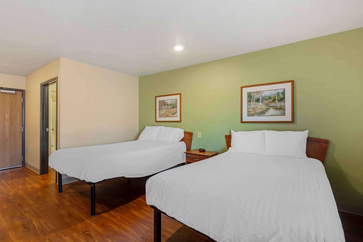 Une chambre d’hôtel avec deux lits simples, un plancher en bois, des murs verts et deux tableaux encadrés.