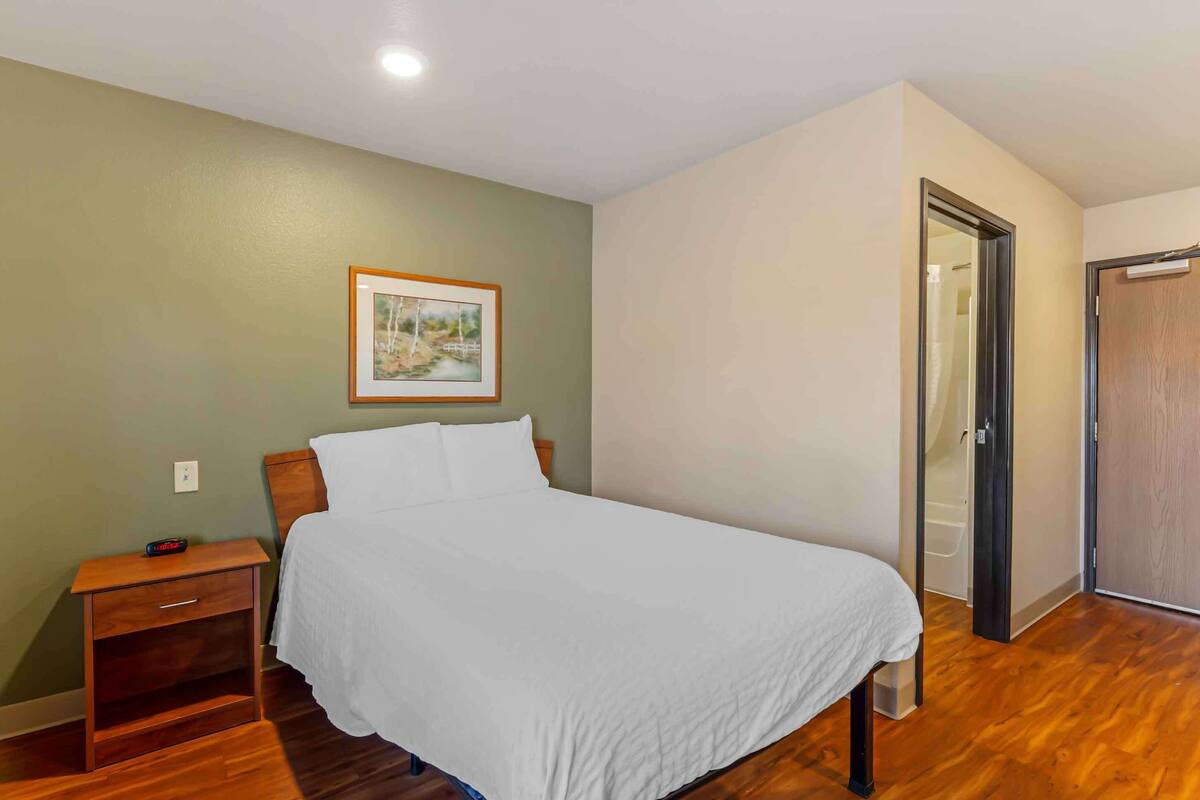 Une chambre à coucher comprenant un lit, une table de chevet et une porte donnant sur une salle de bain.