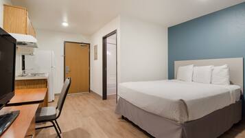 A hotel room with a bed, a desk with a computer, a chair, and a kitchenette.