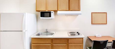 A compact kitchenette with a refrigerator, microwave, sink, stove, and a small table with a chair.