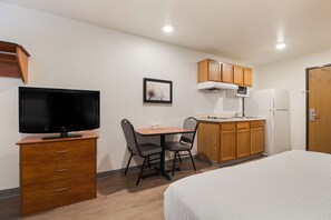 A compact hotel room with a bed, a TV on a wooden dresser, a kitchenette with a microwave and refrigerator, and a small dining table with chairs. - WoodSpring Suites Houston Westchase (Houston)