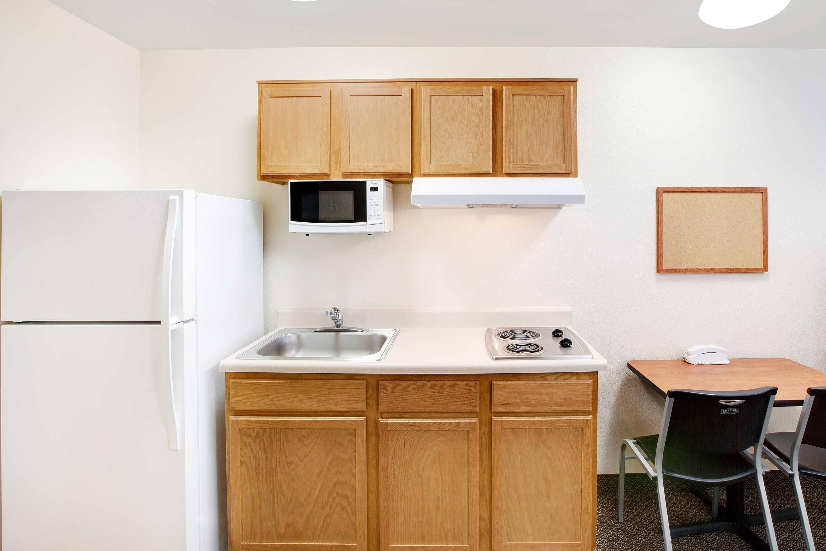 Cocina compacta equipada con refrigerador, microondas, fregadero, estufa y una pequeña mesa con una silla.