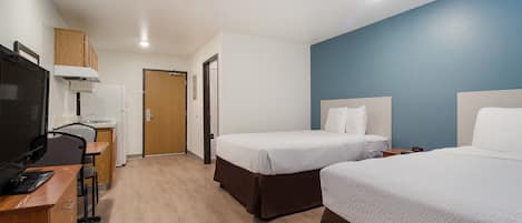 A hotel room with two beds, a desk with a computer, a television, and a kitchenette.