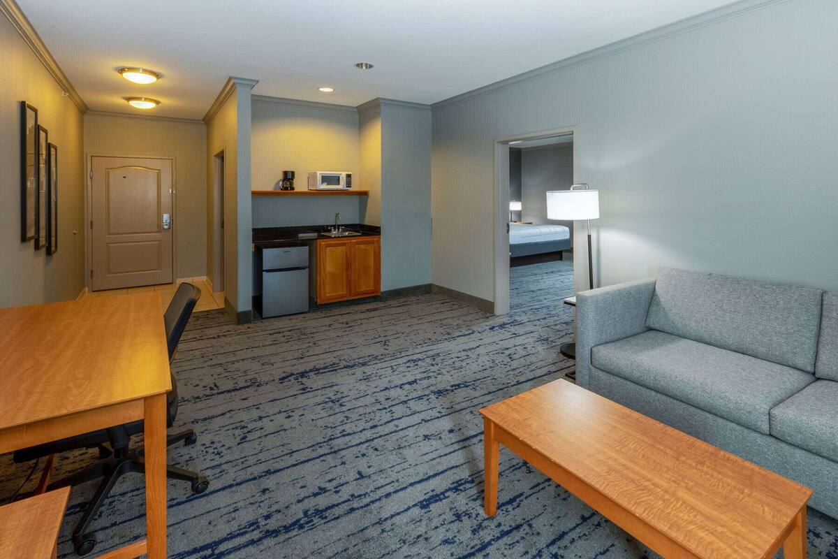 A hotel room with a kitchenette, a sofa, a dining table, and a lamp.