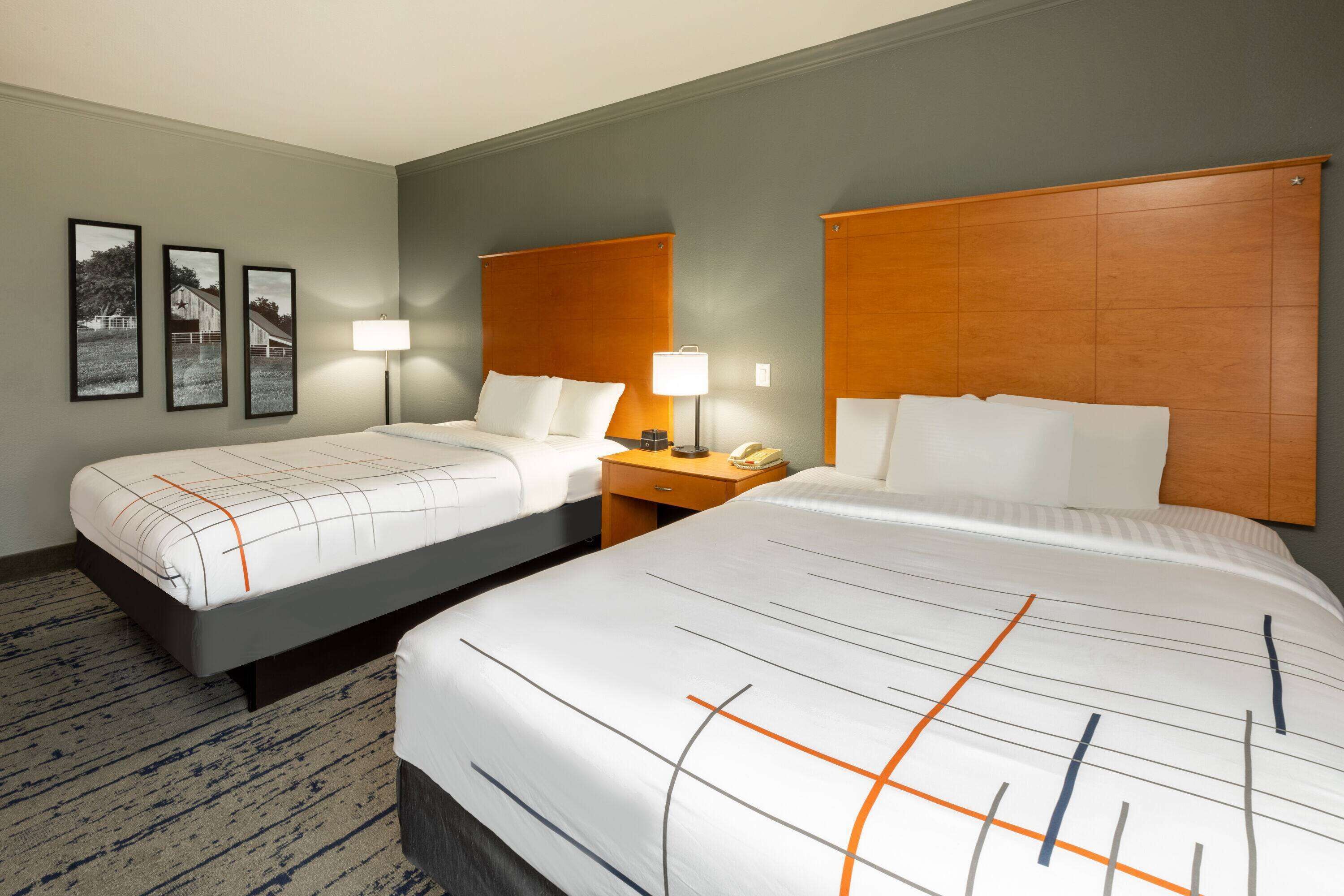 A hotel room with two beds, a nightstand, a lamp, and framed pictures on the wall.