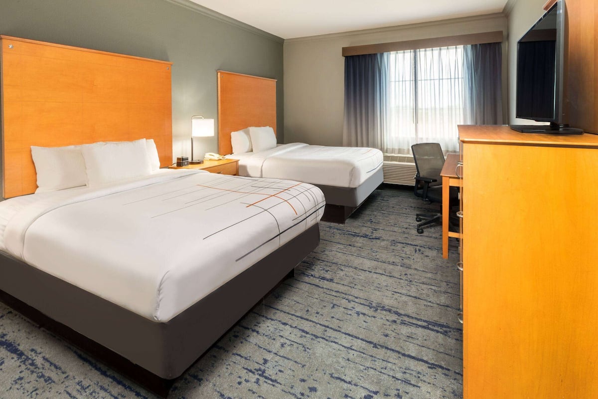 A hotel room with two beds, a desk, a chair, a television, and a window with curtains.