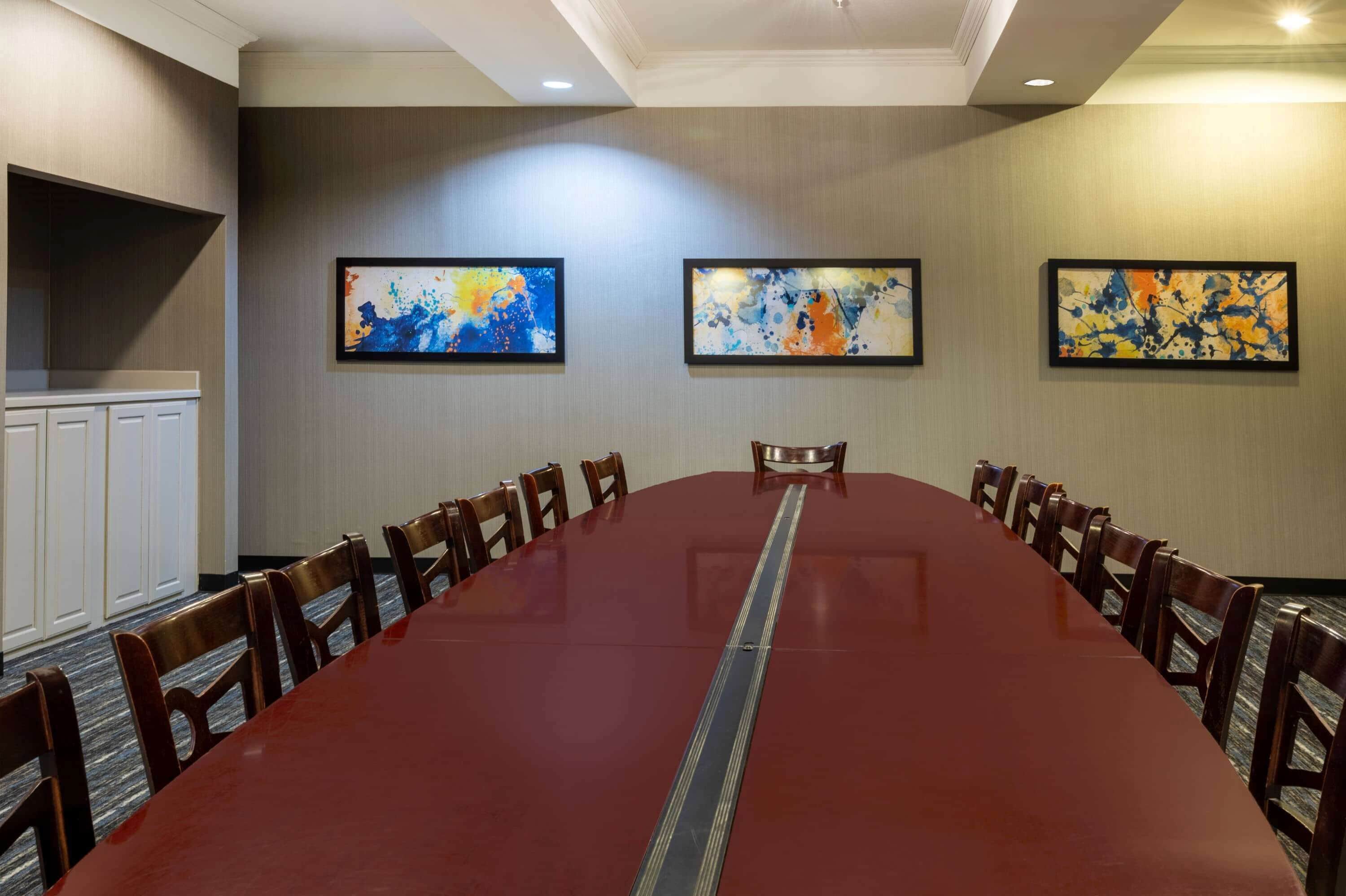 Uma sala de conferências com uma mesa comprida, cadeiras e três pinturas abstratas na parede.