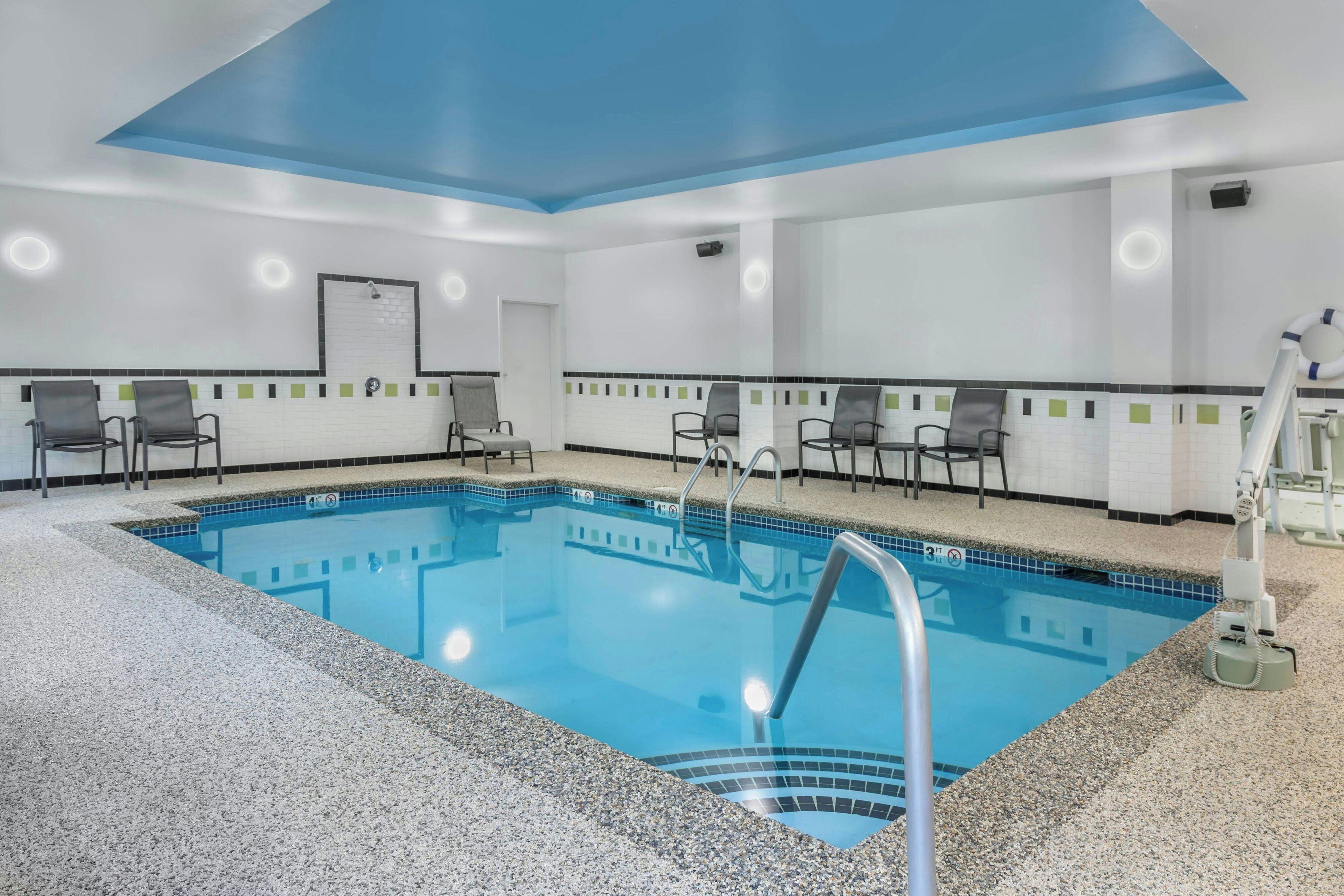 Zona de piscina d'hotel amb una piscina blava cristal·lina, seients al voltant i un sostre amb detall blau.