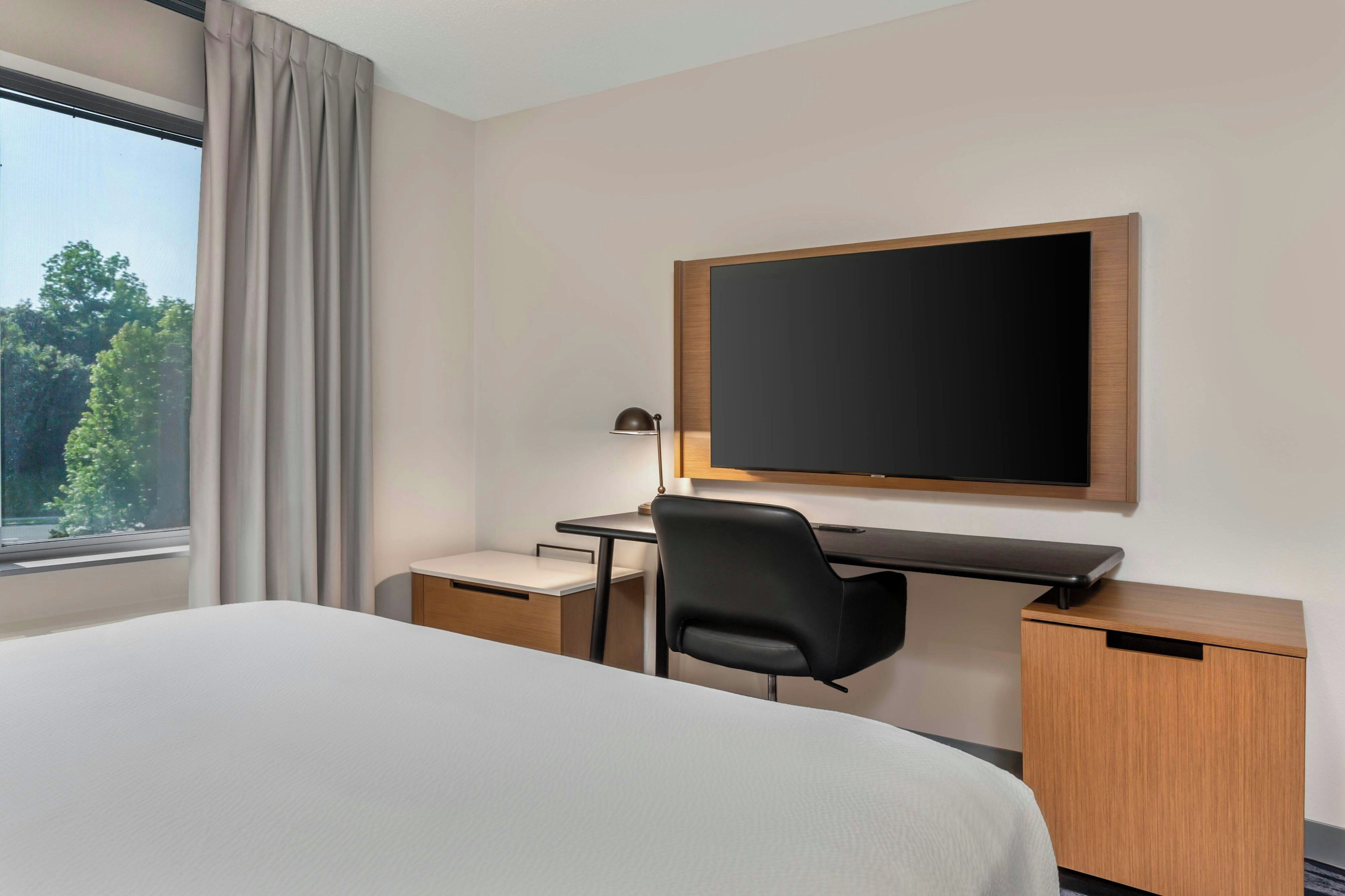 A hotel room with a bed, a desk, a chair, a television, and a window with curtains.