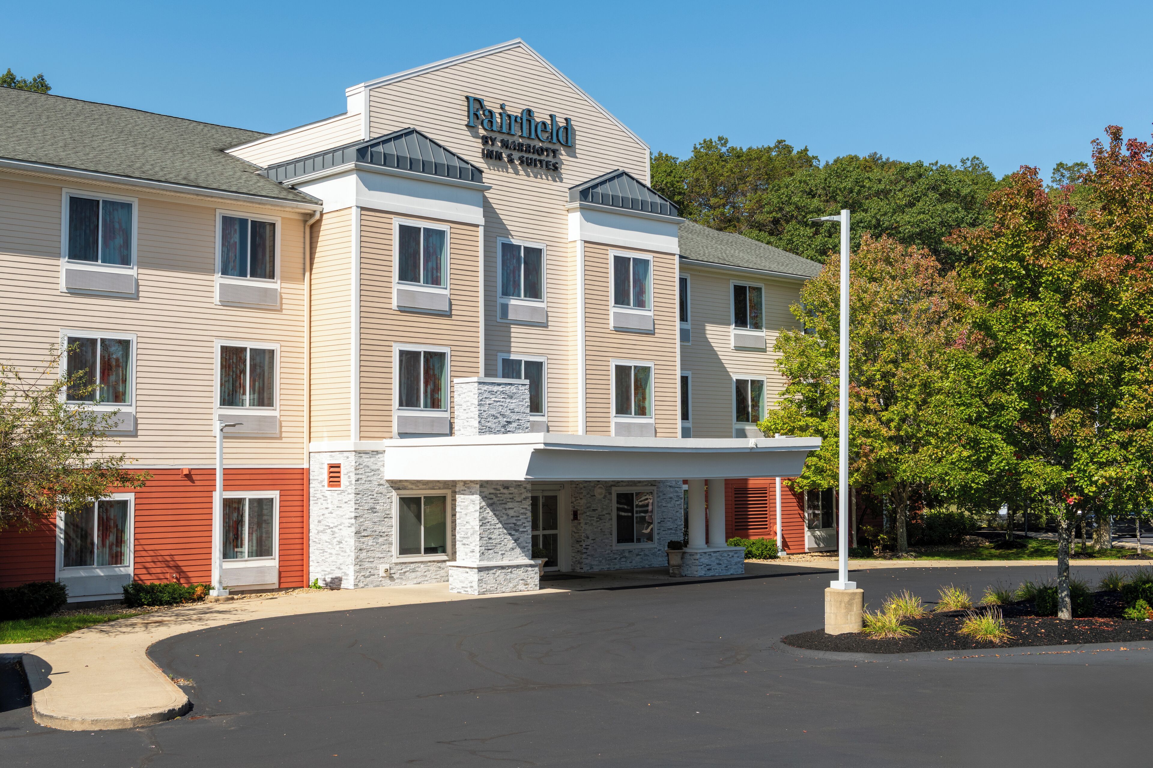 Um hotel com vários andares, um letreiro chamativo, entrada coberta e um acesso por um caminho arborizado.