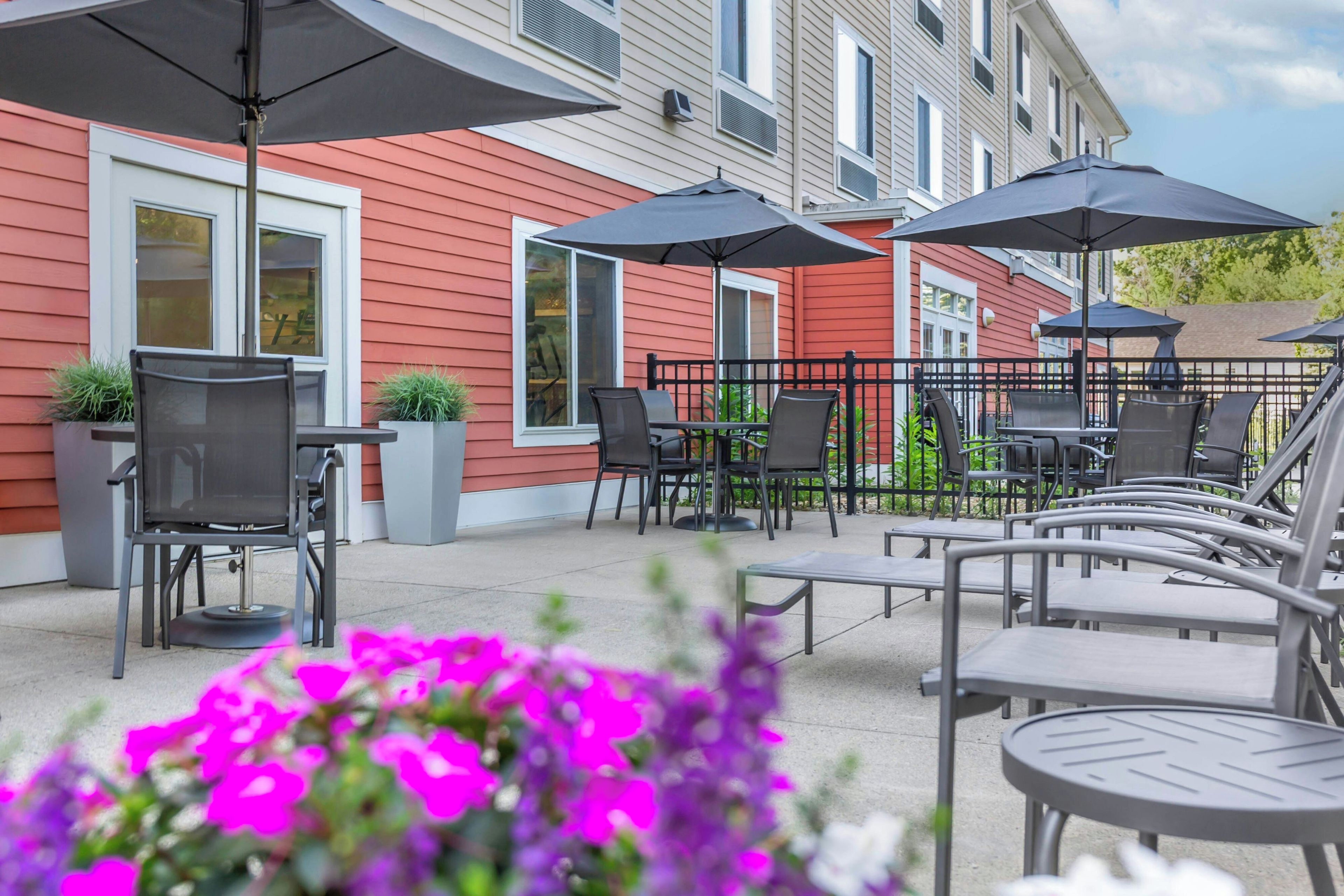 An outdoor patio with multiple tables and chairs, umbrellas, and potted plants.