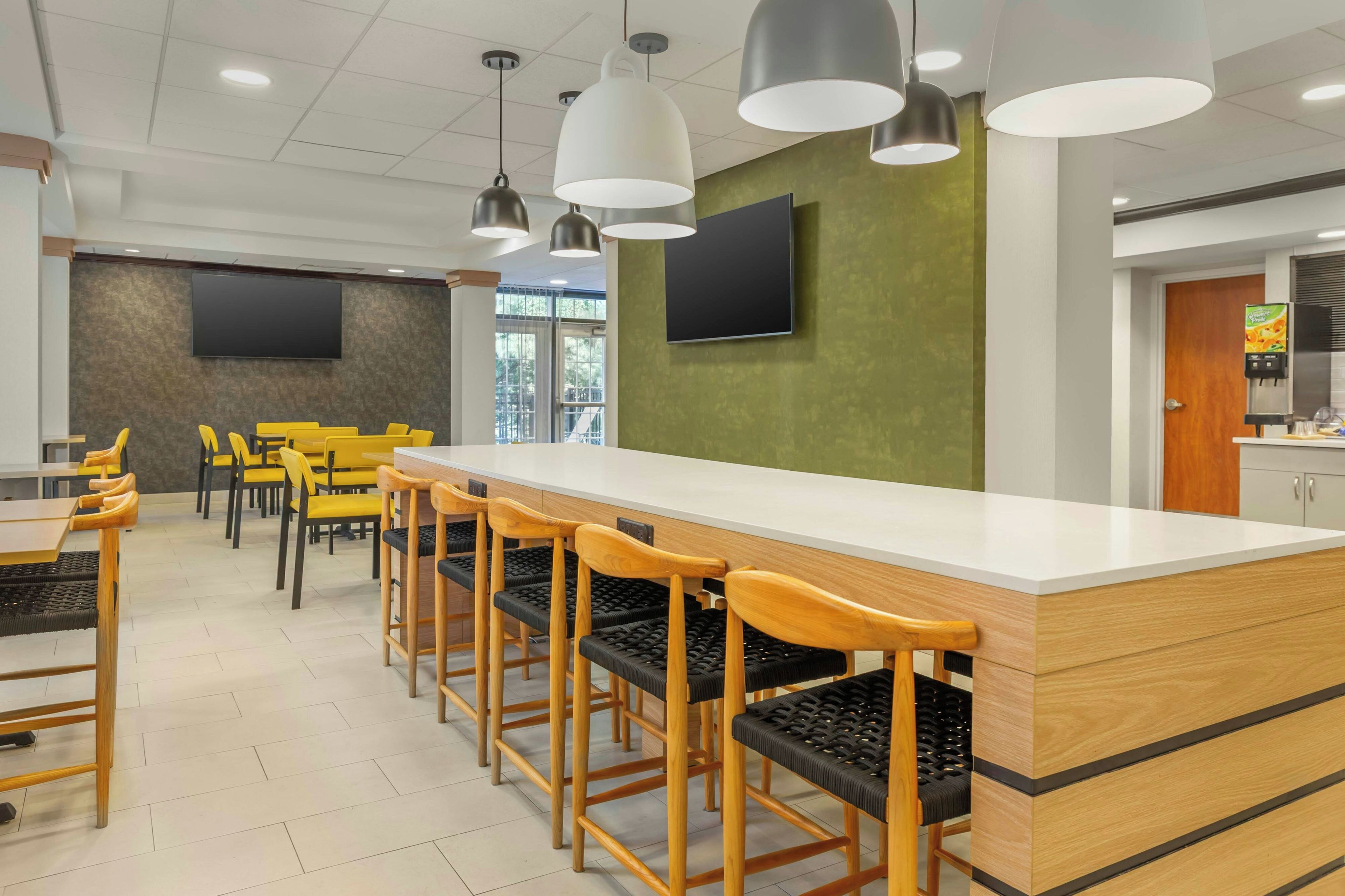 A modern dining area with a long wooden table, yellow chairs, and black cushioned stools.
