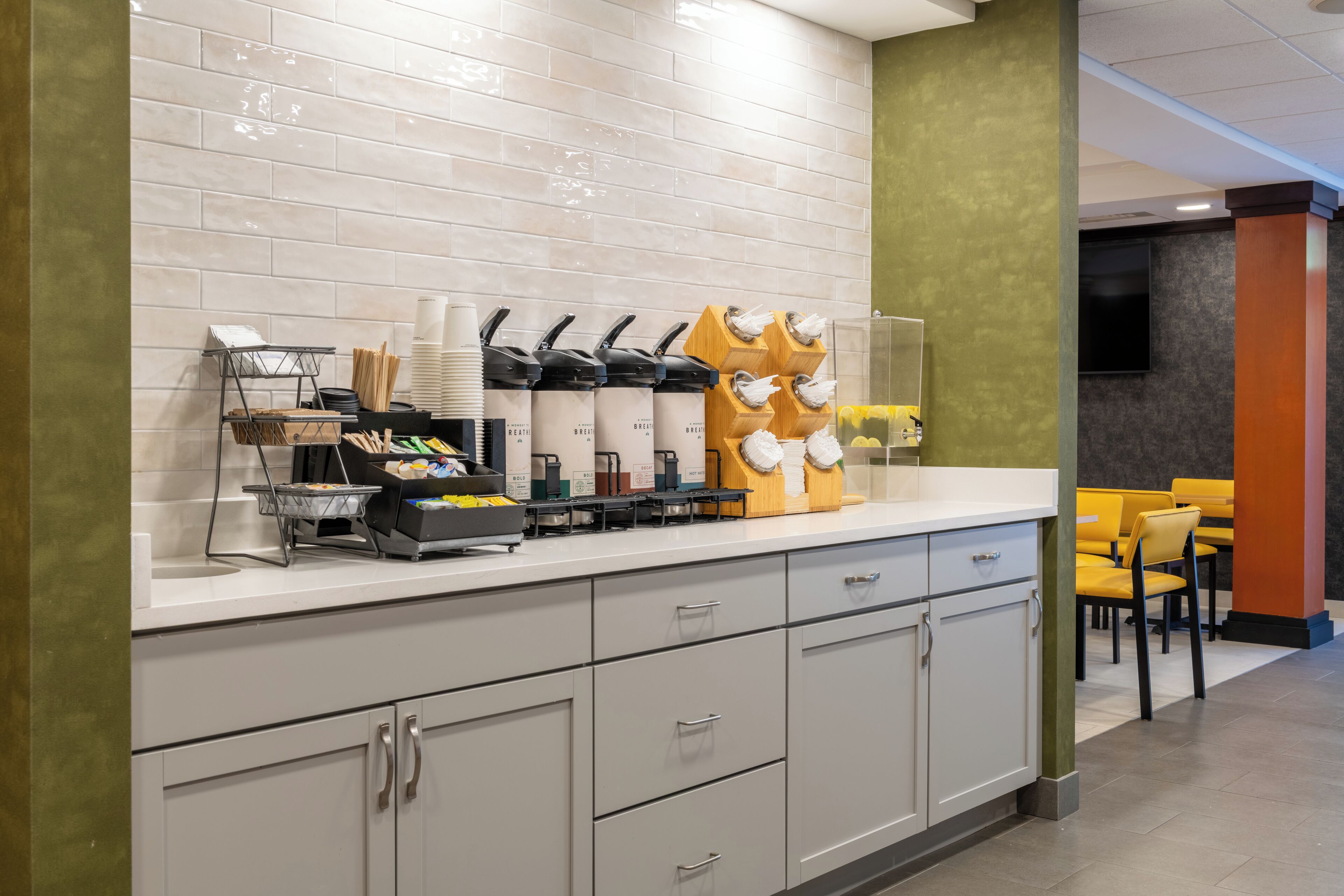 Un espace cuisine moderne avec un plan de travail blanc, divers appareils de cuisine et un coin salon avec des chaises jaunes.