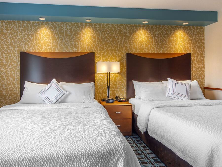 A hotel room with two beds, a nightstand with a lamp, and patterned wallpaper.